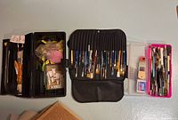 Overall view of three containers holding artist brushes and paint tubes, arranged on a surface