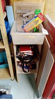 Full view of MDF shelving unit containing art supplies including paint brushes, paint, pencils, a highlighter, and a red notebook.