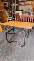 Full view of artist table showing laminate wood-tone top, rectangular shape and black metal frame with tubular legs.