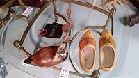 Photo showing the two wooden shoes and the two wooden bird decoys on a glass table, including a large wooden duck signed Country Traditions and smaller red bird decoy.