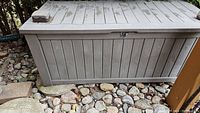 Front view of the outdoor utility storage box sitting on a bed of rocks outdoors, showing the latch and vertical panel details.