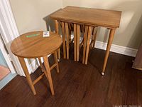 Four teak folding side tables beside larger wheeled teak storage table