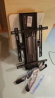 Full view of black metal TV wall mount bracket with attached mounting arms and central cover plate, lying on floor against wall