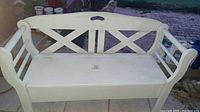 Front view of the white wooden bench with crisscross slat backrest and rounded armrests.