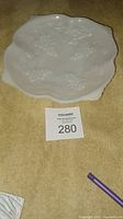 Top view of milk glass candy dish showing grape and leaf embossed pattern and scalloped edges.