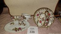 Full view of three cups, two salt and pepper shakers, oval tray and saucers showing floral rose motifs and gold trim