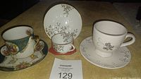 Photo showing three coffee cups and their matching saucers placed on a yellow surface with lot number card in front