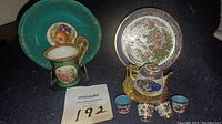 Photo of six cups and saucers each displayed on gold-colored stands with varied floral and scenic designs