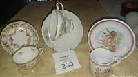 Photo showing three ceramic cup and saucer sets with stands: one from Japan and two from Germany with distinct floral and bird designs.