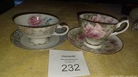 Frontal photo showing two floral design cups and matching saucers placed on yellow fabric.
