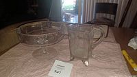 Photo of heavy glass pitcher and glass candy dish on table showing clear glass with edged design on pitcher and smooth pedestal candy dish.
