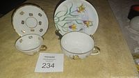 Two porcelain tea cups and two saucers, one set decorated with lilies, the other with gold emblems.