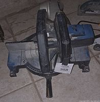 Top-down view of electric cut off saw showing black handle, blue motor housing, and angle adjustment markings on metal base.