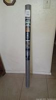 Full view of wrapped roll of gray commercial weed control fabric standing upright against a wall