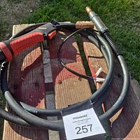 Photo showing red and black wire feed handle with attached black welding cable coiled on wooden surface