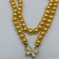Close-up of golden pearls and butterfly clasp showing crystal detail