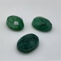 Three faceted oval emeralds on white background, overhead view