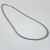 Full length of the flat herringbone chain necklace laid out on white surface showing chain style and length.