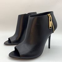 Front and side angled view of black leather peep-toe stiletto booties with gold zippers on the side.