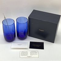 Two blue glasses, pearl stirrer, black Mikimoto box and accompanying cards displayed on a table with white background.