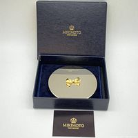 Mikimoto branded navy blue box with velvet interior holding the closed compact mirror.