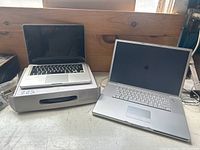 Two silver Apple MacBook laptops side by side, one on a box, one on the table
