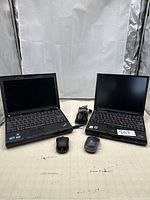Two Lenovo ThinkPad laptops side by side with their wireless mice and power cords visible in front.
