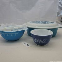 Three blue and white Pyrex bowls and one covered casserole dish in blue and white with snowflake and floral patterns