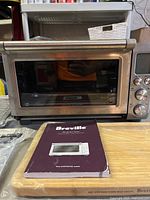 Stainless steel Breville Smart Oven on table with bamboo cutting board and instruction manual in front