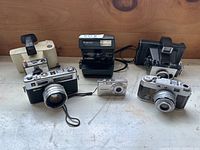 Lot of six cameras arranged on a table including vintage and digital models.