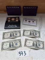 Mixed lot showing two purple cases each holding a 1992 United States Mint Proof Set, a black case with the 1993 Silver Proof Set, a plastic holder with the heritage coin collection, and four one-dollar bills.