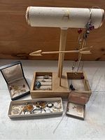 Image showing entire jewelry display including wooden stand with arrow design, necklaces, rings in ring holder, multiple boxed pins, and assorted vintage watches laid out in front.