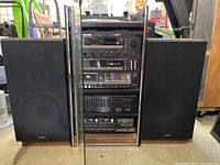 Full view of Fisher stereo unit with glass front, showing multiple stacked components and the two large Technics speakers on each side.