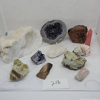 Front view of the full group showing all 10 geodes, minerals, and rocks displayed on white surface and backdrop.