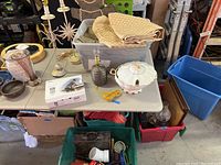 Wide view of the lot showing lamps, linens in a bin, candle holders, decorative gingerbread man, and other home decor items