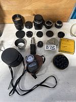 Lot layout showing all camera lenses, caps, film reel canister, and handheld light meter