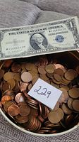 Tin filled with copper pennies and partially visible silver certificate note behind; small lot number card in view