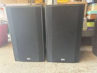 Pair of black EPI speakers with fabric front grilles placed on a concrete floor, showing some dust and signs of wear.