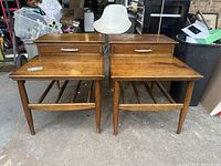 Pair of mid-century modern wooden end tables side by side, showing tops, drawer fronts, tapered legs and horizontal supports.