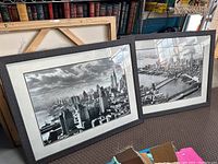 Both framed black and white photographic prints leaning against bookshelves showing two different iconic New York City views.