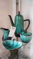 Photo showing full set of Blue Mountain Pottery items including coffee pot, cream pitcher, sugar bowl, and spade dish on glass shelf.