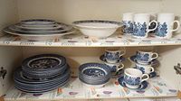 Shelved set of dinner plates, soup bowls, and teacups with saucers in blue and white Churchill Royal Oak pattern.