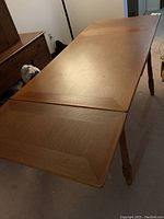 Full view of oak dining table extended with both end leaves inserted, showing turned legs and table top surface.