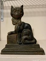 Front view of cast iron cat door stop showing the cat with one eye winking, bow tie, and portion of the base block with text.
