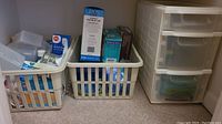 Overview of health aids items packed in plastic baskets and drawer unit, showing Bios blood pressure monitor box and other supplies.
