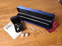 Photo showing the bracelet in a blue box, twisted earrings on a black display, necklace chain, and a small red pouch.