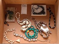 Overview of assorted costume jewelry including multiple necklaces, a few bracelets, and a pair of clip-on earrings displayed in a box