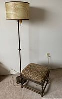 Full view of the tall vintage cast iron floor lamp with attached drum shade in marbled water pattern next to the antique padded foot stool