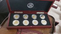 Full set of eight O Canada silver-plated medallions in wooden presentation case with black velvet interior and two brochures.