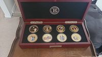 Full view of the wooden display case showing all 8 coins arranged in two rows inside black velvet lining.